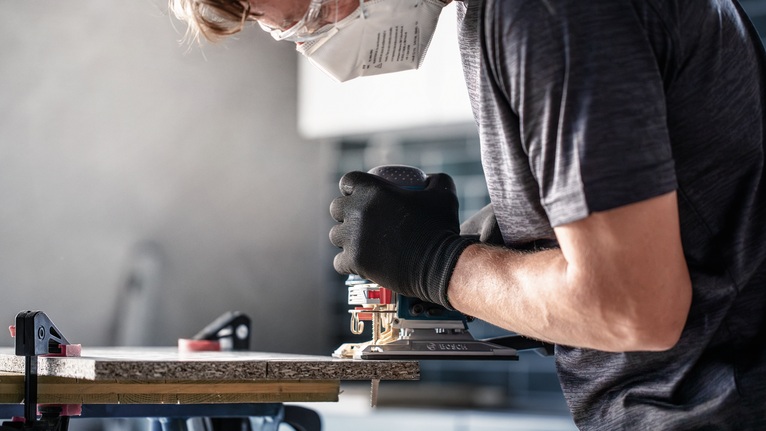 佩戴安全设备的人员使用电动工具切割木材。.