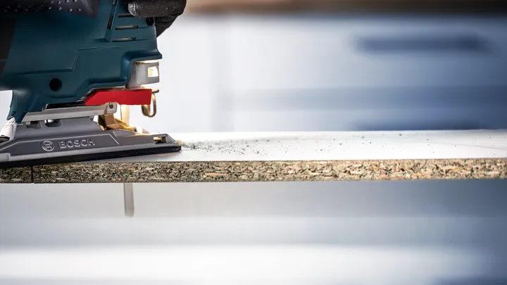 佩戴安全设备的人员使用曲线锯切割层压板。.