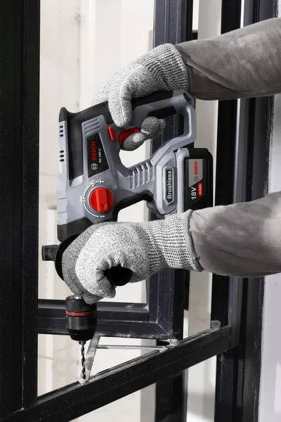 一名佩戴安全设备的人员使用无绳旋转锤在金属框架上钻孔。