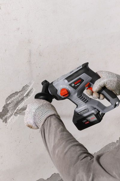 一名佩戴安全设备的人员正在使用电动凿子清除墙上的灰泥。