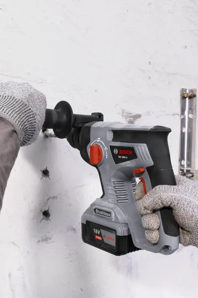 一名佩戴安全设备的人用无绳旋转锤在墙上钻孔。