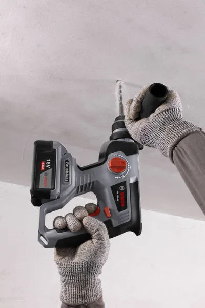 一名佩戴安全设备的人用无绳旋转锤在天花板上钻孔。