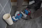 一名佩戴安全设备的人员使用多功能工具切割管道旁边的地砖。