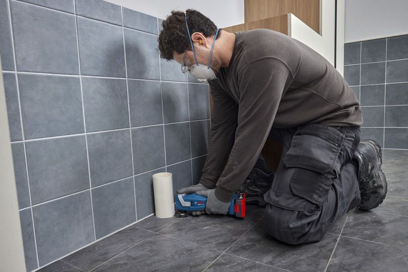 一名佩戴安全设备的人员使用多功能工具切割地砖。