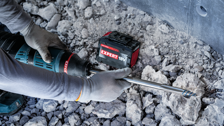 佩戴安全设备的人员在岩石地面上操作无绳旋转锤。