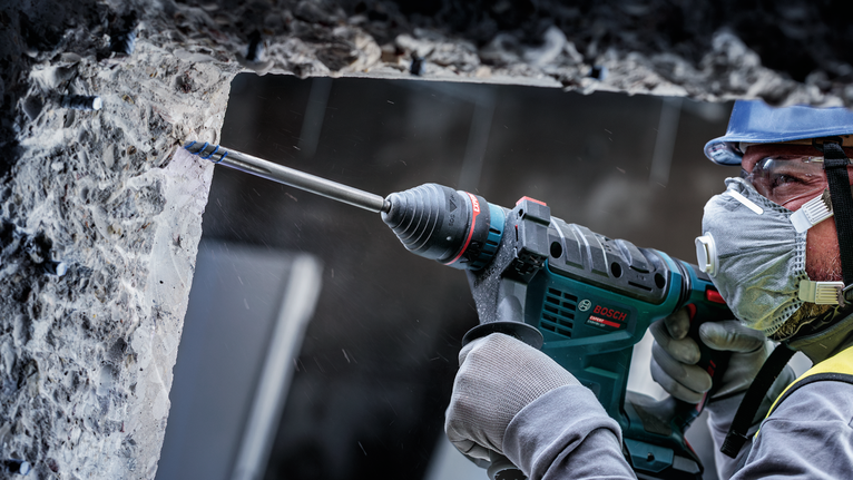 一名佩戴安全设备的人正在钻入混凝土墙。