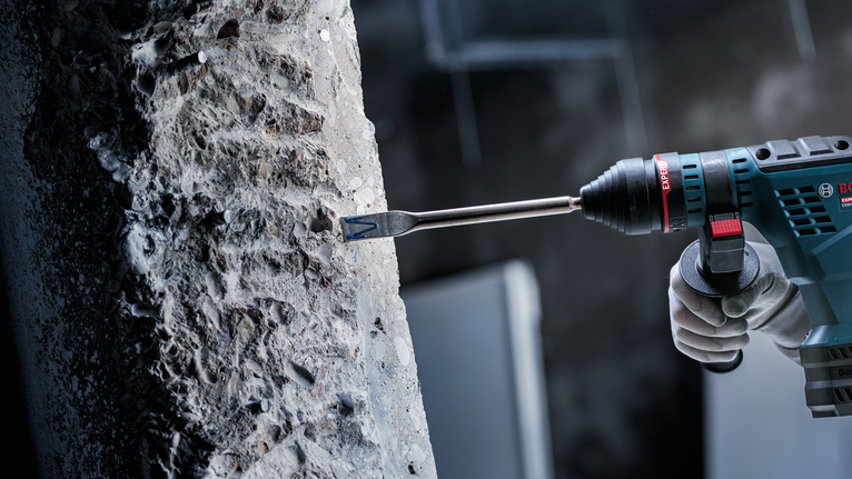 佩戴安全设备的人员使用旋转锤钻凿混凝土。