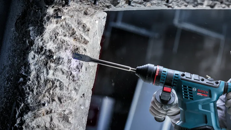 佩戴安全设备的人员使用电动工具凿混凝土。