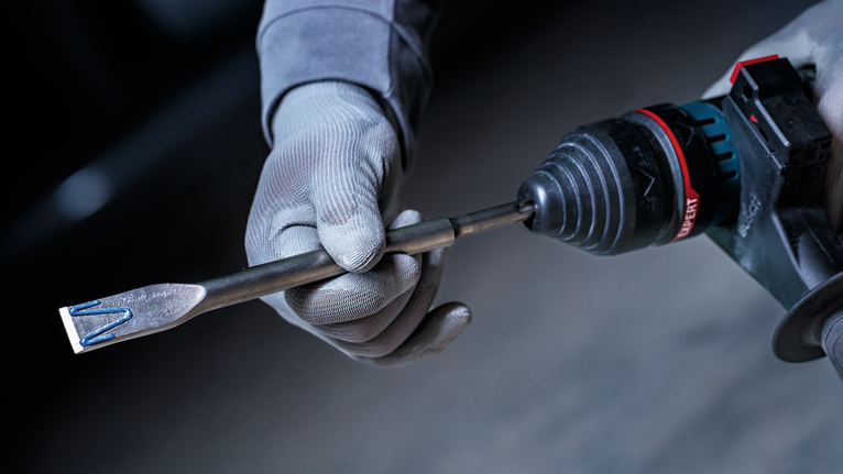 佩戴安全设备的人员手持装有凿子钻头的旋转锤钻。