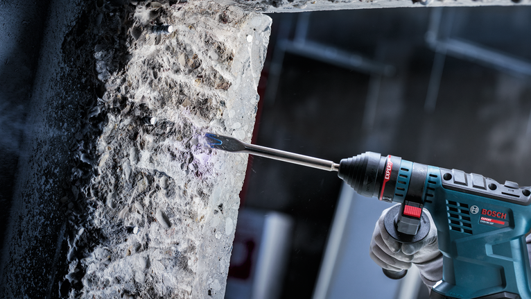 佩戴安全设备的人员使用旋转锤凿开混凝土。