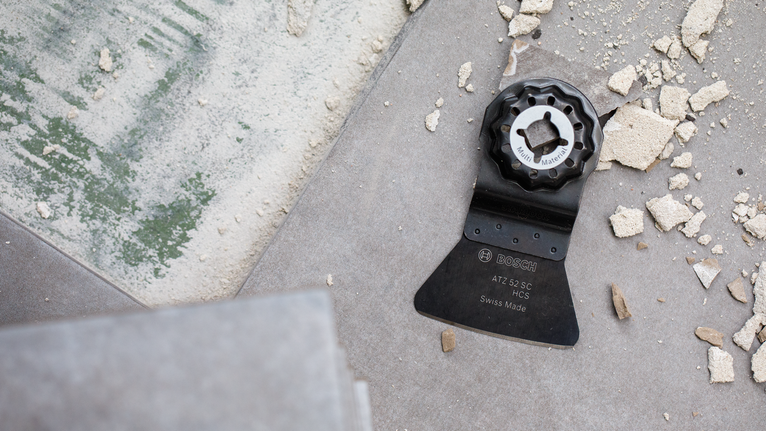 振动式多功能工具刀片位于瓷砖地板上，周围都是建筑垃圾。