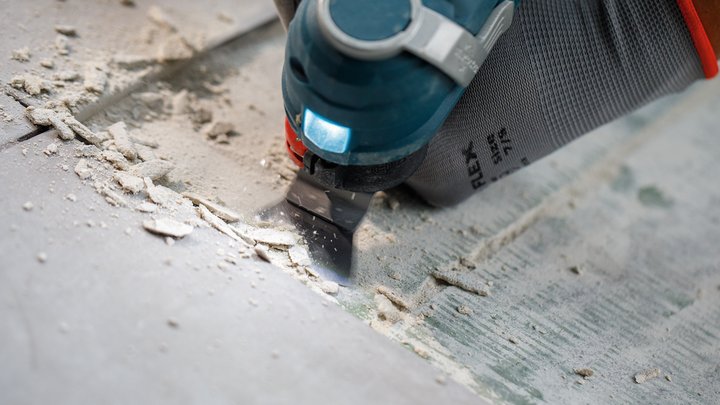 一名佩戴安全设备的人员使用多功能工具去除瓷砖粘合剂。