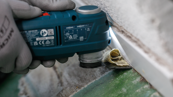 佩戴安全设备的人员使用电动工具切割靠近墙壁的管道绝缘层。