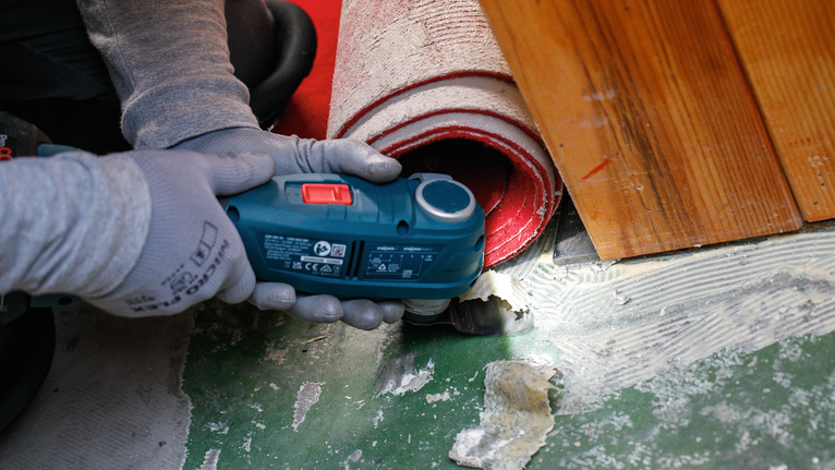 佩戴安全设备的人员使用电动工具切割卷起的地毯附近的地板。