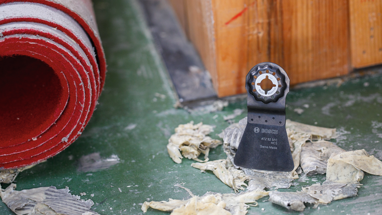 振荡工具刀片直立在红色卷起地毯附近的绿色地板上。