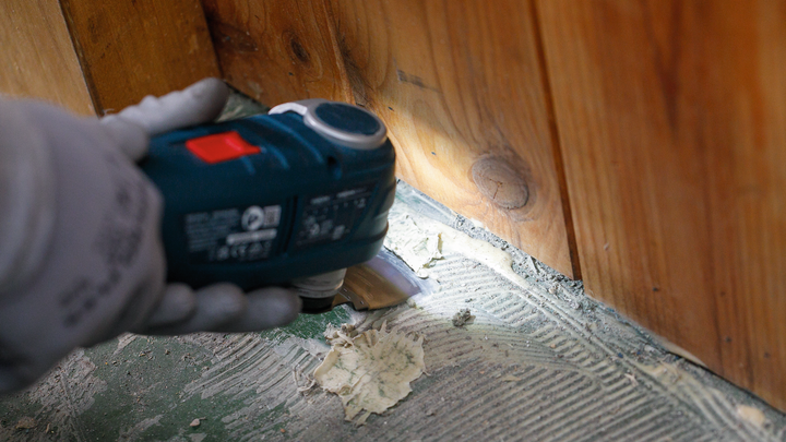 佩戴安全设备的人员使用电动工具从地板上刮掉旧粘合剂。