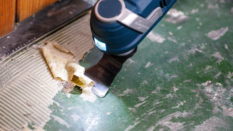 使用电动工具从绿色地板表面刮掉粘合剂。
