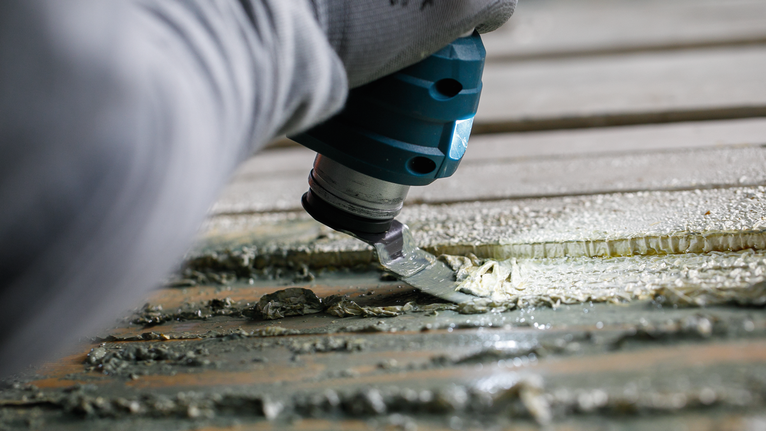 佩戴安全设备的人员使用多功能工具从表面刮掉粘合剂。