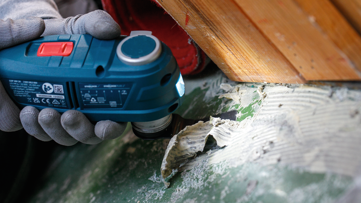 一名佩戴安全设备的人员使用电动工具去除粘合剂残留物。