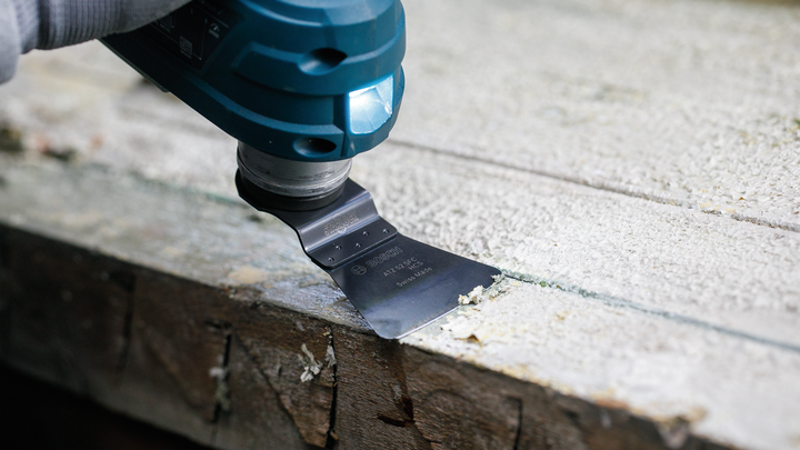 一名佩戴安全设备的人员使用多功能工具从木头上刮下材料。