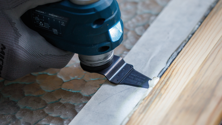 佩戴安全设备的人员使用多功能工具沿着木头边缘切割。