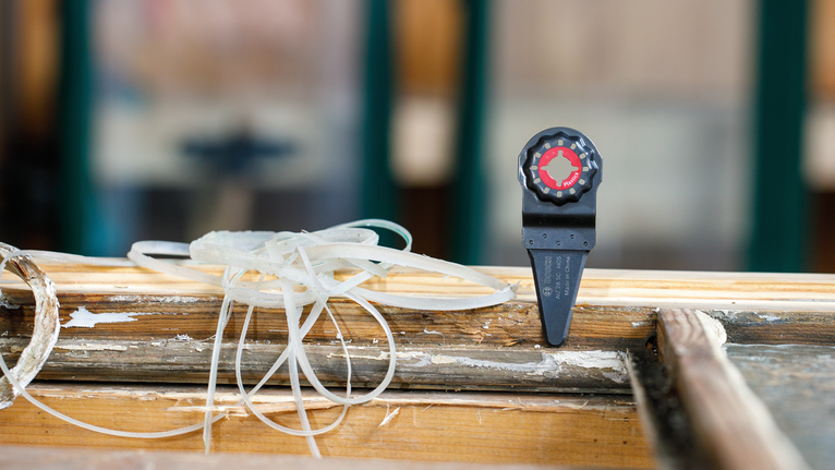 振荡工具刀片附件放置在带有刨花的磨损木质表面上。