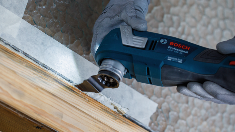 一名佩戴安全设备的人员使用电动工具打磨木制窗框。