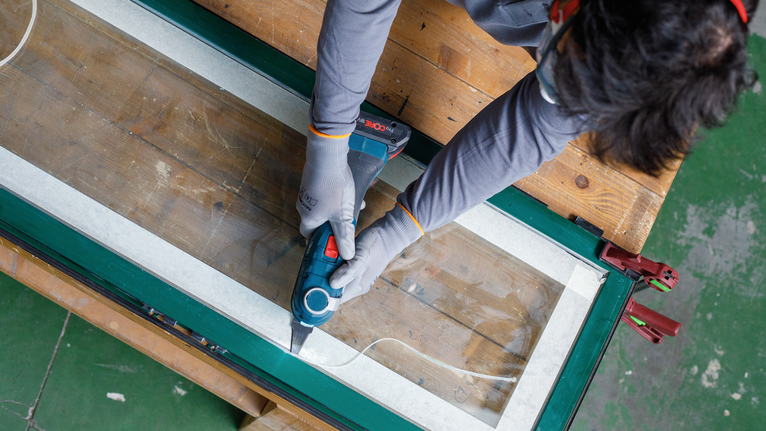 佩戴安全设备的人员使用电动工具切割窗框。