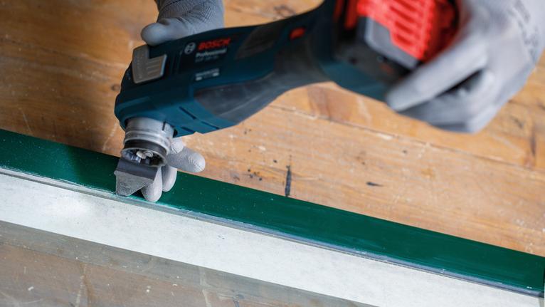 佩戴安全设备的人员使用无绳多功能工具打磨已涂漆的窗框。