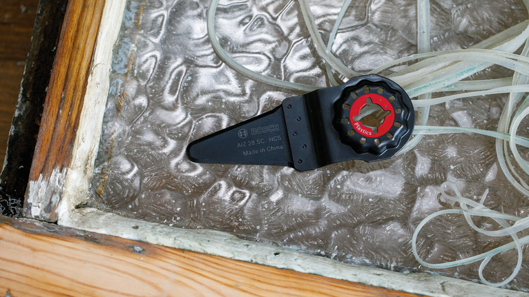 振动工具刀片放置在磨损的窗户密封条旁边。