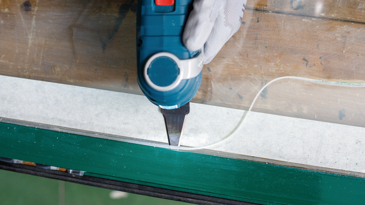 佩戴安全设备的人员使用电动工具从窗框上去除密封剂。