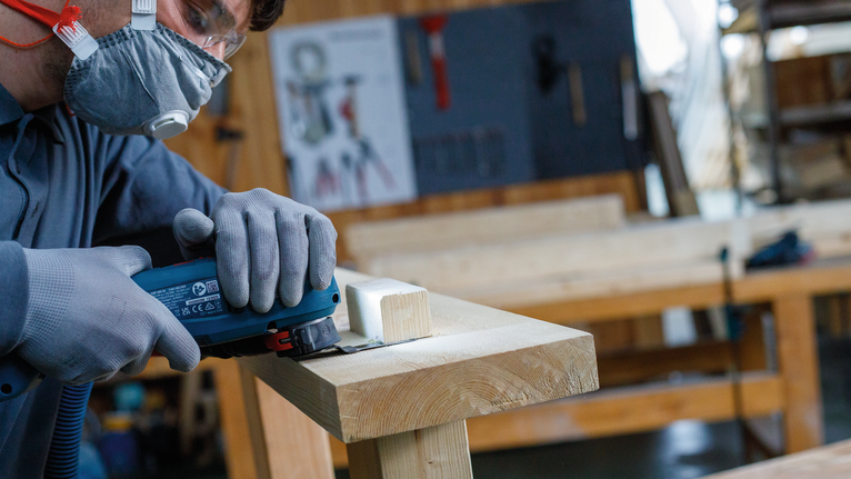 车间里，一名佩戴安全设备的人员正在使用电动工具切割木材。