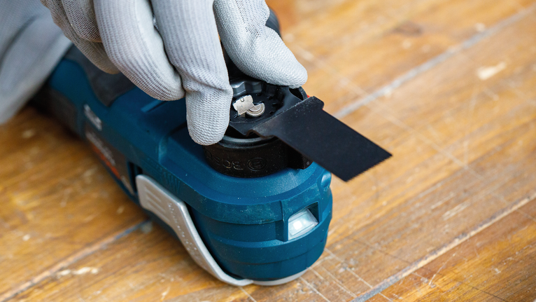 佩戴安全设备的人员将工具刀片安装到木质表面上的电动工具上。