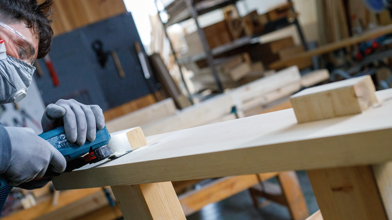 佩戴安全设备的人用电动工具打磨木板。