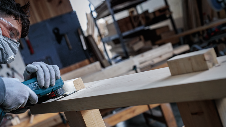 一名佩戴安全装备的人员在车间里打磨木板。