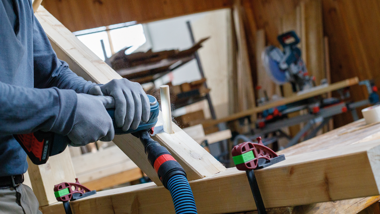 一名佩戴安全设备的人员在车间内钻入一块木板。