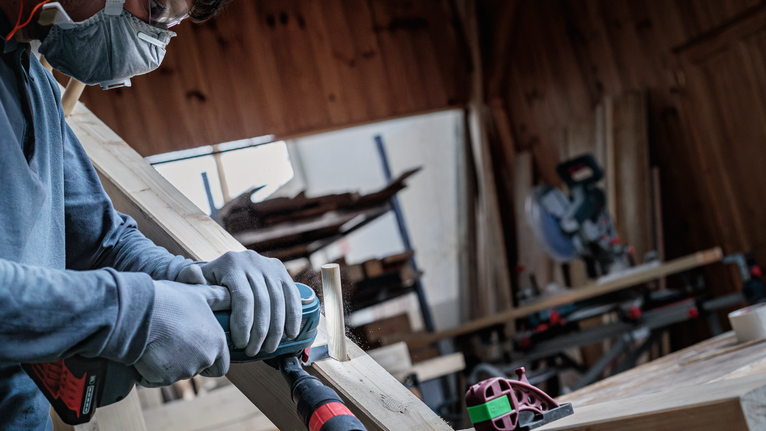 一名佩戴安全装备的人员正在用电动工具打磨木板。