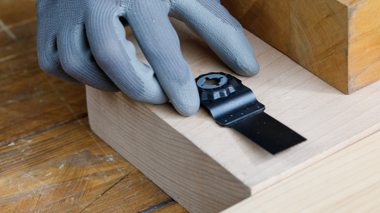 佩戴安全设备的人员将多功能工具刀片放置在木质表面上。