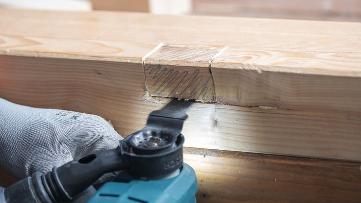 佩戴安全设备的人员使用电动工具切割木梁。