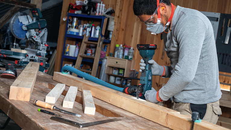 一名佩戴安全设备的人员在车间内钻木梁。