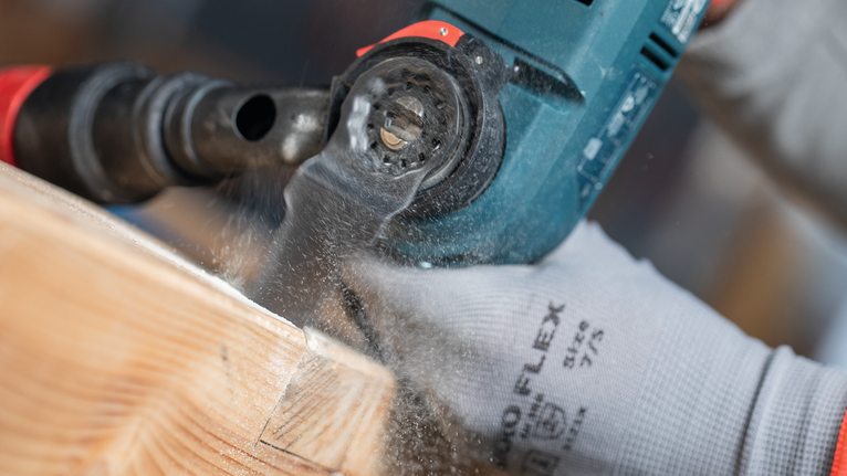 佩戴安全设备的人员在木梁上钻孔，产生锯末。