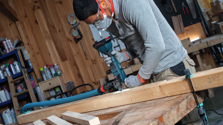 佩戴安全设备的人员在工作台上的木梁上钻孔。