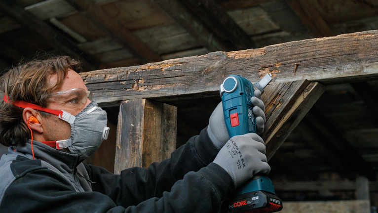 一名佩戴安全设备的人员使用无绳工具打磨木梁。