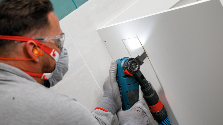 佩戴安全设备的人员使用电动工具在面板上切出一个矩形孔。