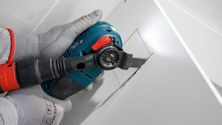 佩戴安全设备的人员使用电动工具在干墙上切出一个矩形开口。