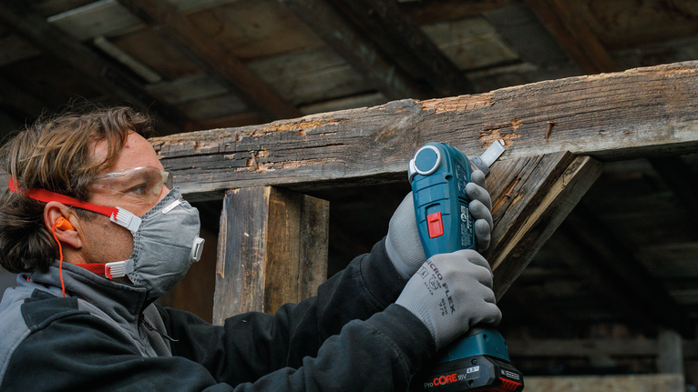 佩戴安全设备的人员使用电动工具打磨木梁。