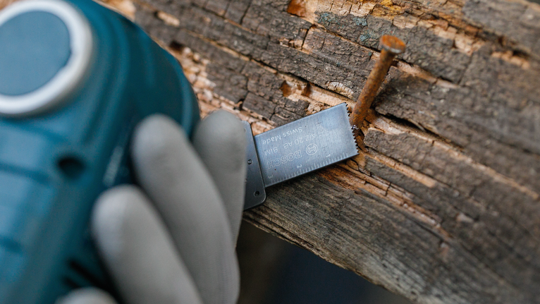 穿着安全设备的人在生锈的钉子附近用电动工具切割木材。