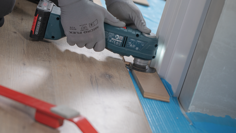 穿着安全设备的人员正在修剪门框附近的复合地板。