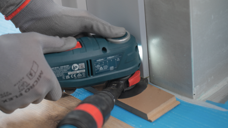 佩戴安全设备的人员操作多功能工具切割金属表面附近的地板。