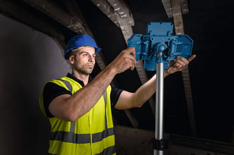 一名佩戴安全装备的工人正在调整支架上的无线工地照明灯。